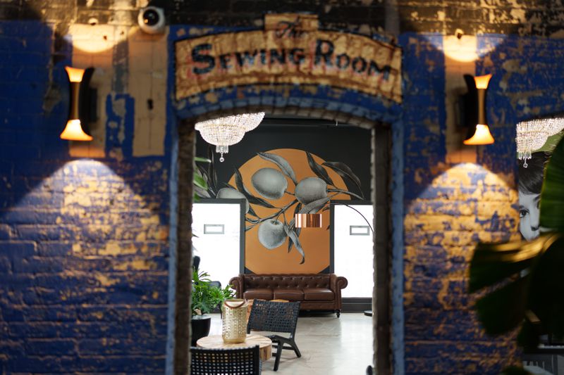 An archway in a wall that’s painted blue and says “sewing room” with a couch in the next room.