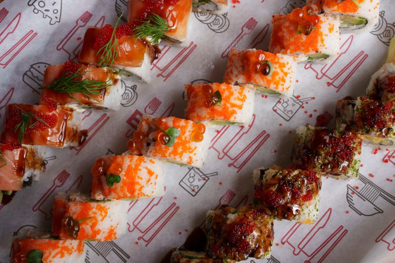 Three rows of sushi on white paper with a red and black design.