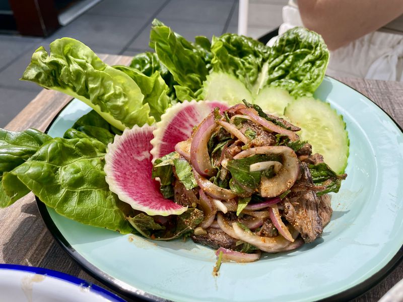 Beef larb with lettuce leaves, radishes, and cucumbers on a blue plate.