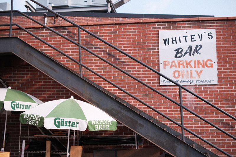 A painted sign that says “Whitey’s Bar Parking only” posted on a brick wall, with a set of stairs in front of the brick wall. 