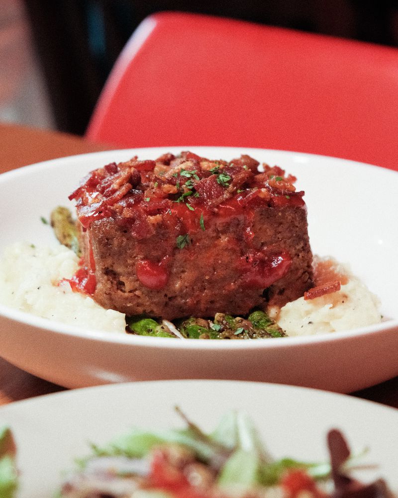 A piece of meatloaf over mashed potatoes in a white dish. 