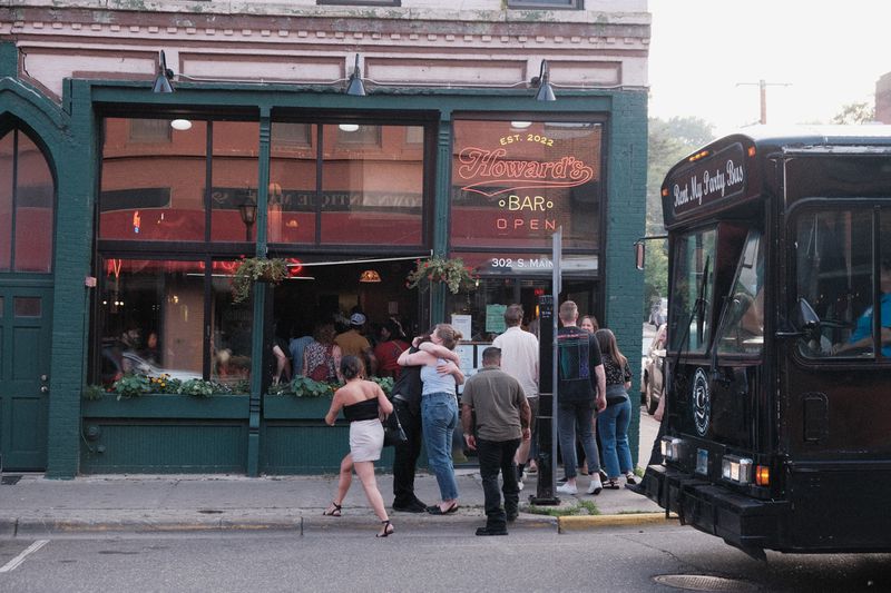 People standing and hugging outside the brick exterior of Howard’s Bar, with a black bus to the right. 