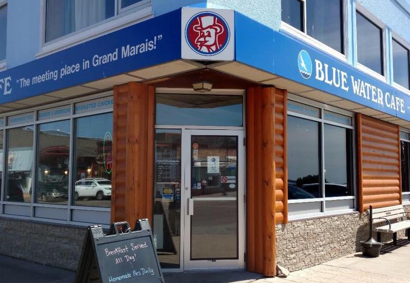 A storefront with windows and glass door and a blue awning that says “Blue Water Cafe.”