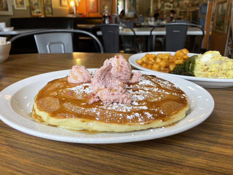 Two pancakes topped with pink butter on a white plate. 