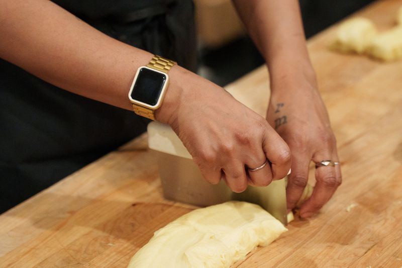 Two hands with rings and watch cutting dough on a wooden counter. 