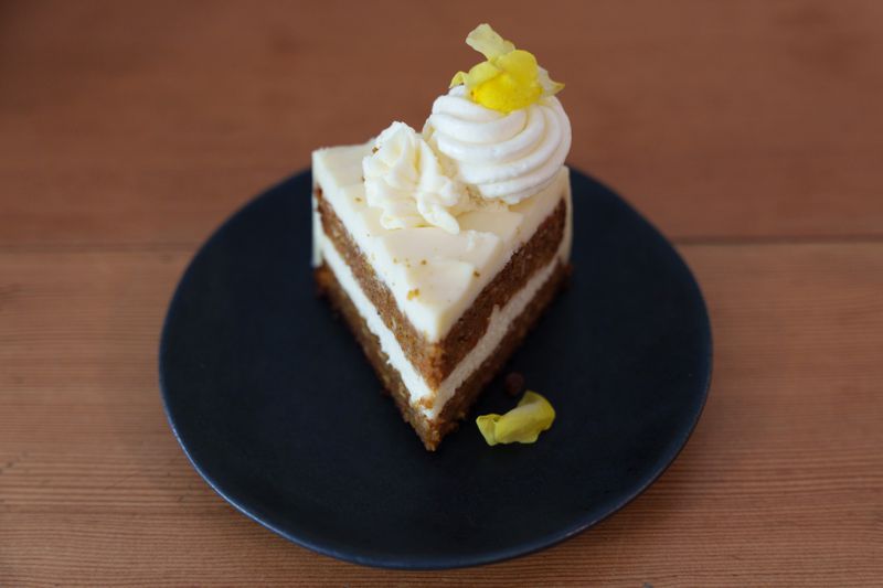 A slice of tahini carrot cake on a black plate on a wooden table. 