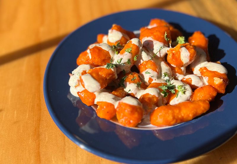 A round blue plate of cheese curds covered in buffalo sauce and drizzled with ranch. 