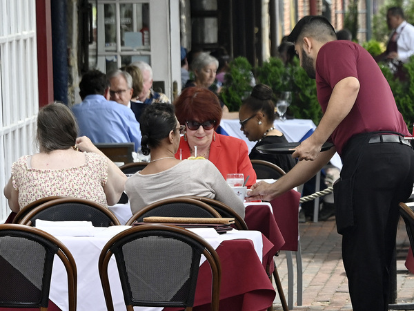 A waiter works at a restaurant in Alexandria, Va., on June 3, 2022. Consumers continue to spend on services like eating out. That helps the economy and the labor market, but it also keeps inflation high.