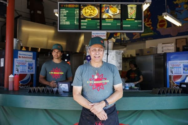 a man with green t shirt and green cap poses in front of a booth