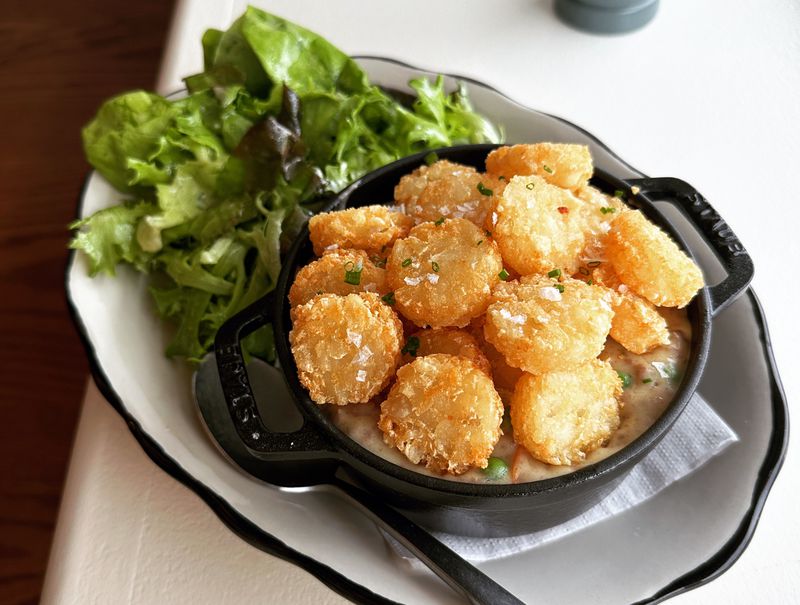 A small iron skilled of hotdish topped with tater tots on a white plate. 