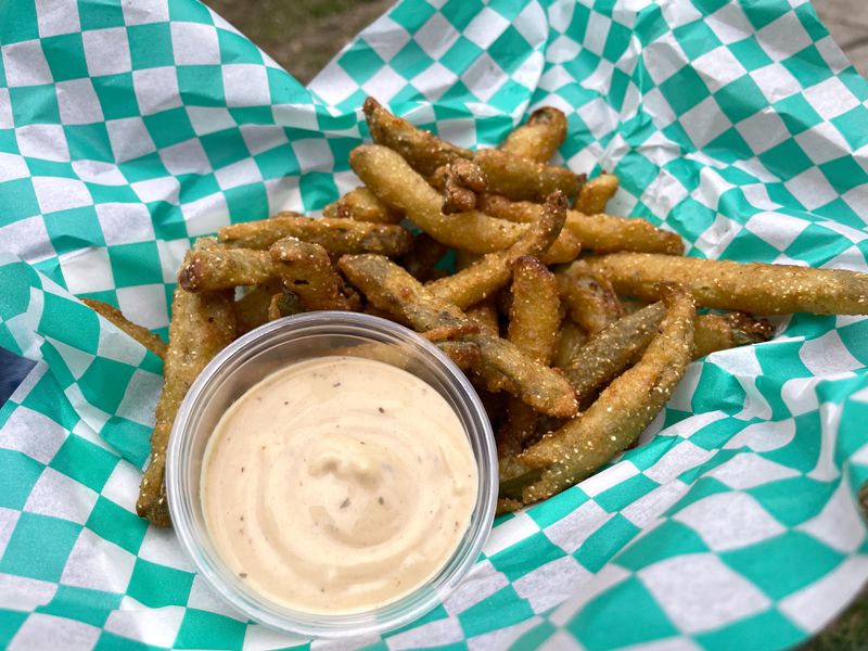 A basket of pickle fries with a creamy chipotle sauce on green and white checked paper.
