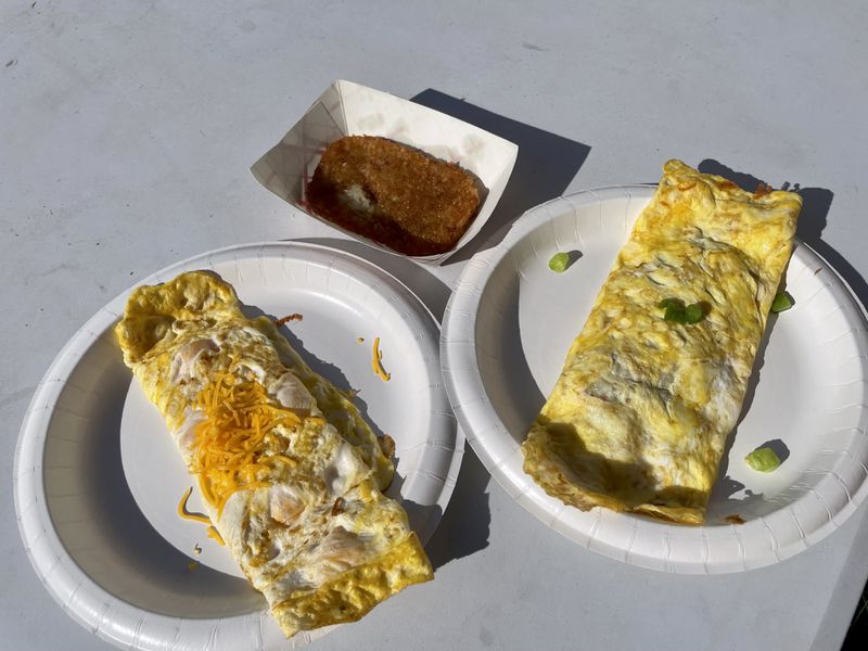 Two omelets on white paper plates and a small paper boat with a hashbrown patty in it. 