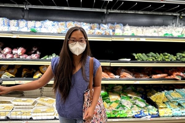 a woman wearing a mask stands in front of a supermarket aisle