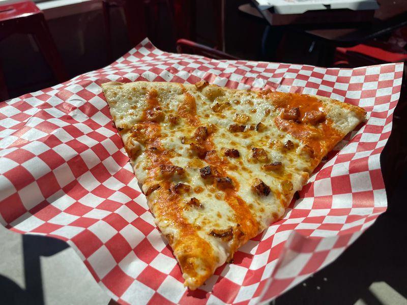 A slice of buffalo chicken pizza on a red and white checkered piece of paper. 