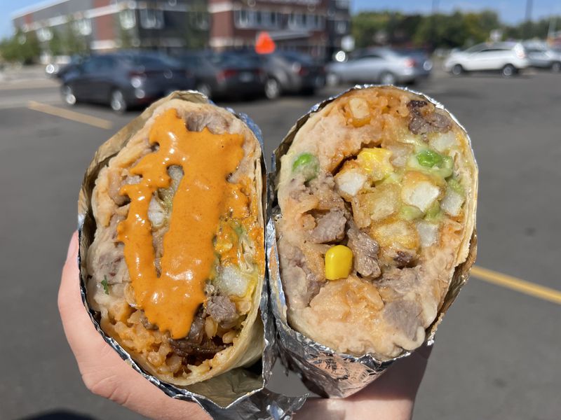 A hand holding a burrito cut in half, stuffed with french fries, steak, and vegetables. 