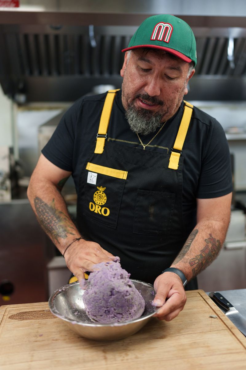 Gustavo Romero mixing together mashed purple potatoes and blue corn masa in a silver bowl. 