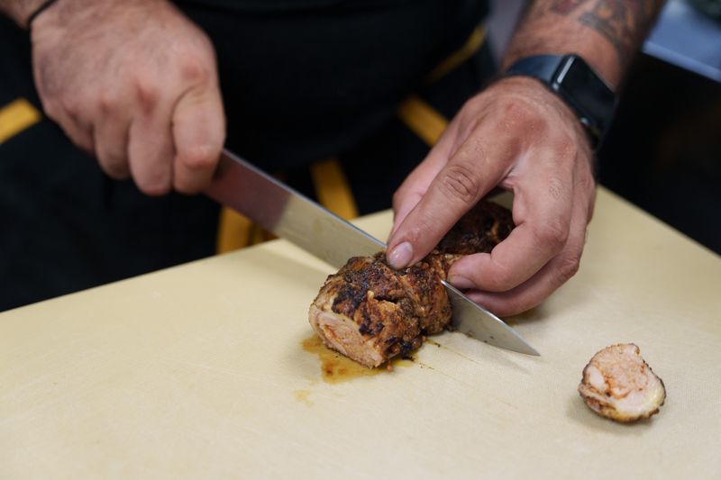 Hands slicing chicken on a yellow cutting board. 