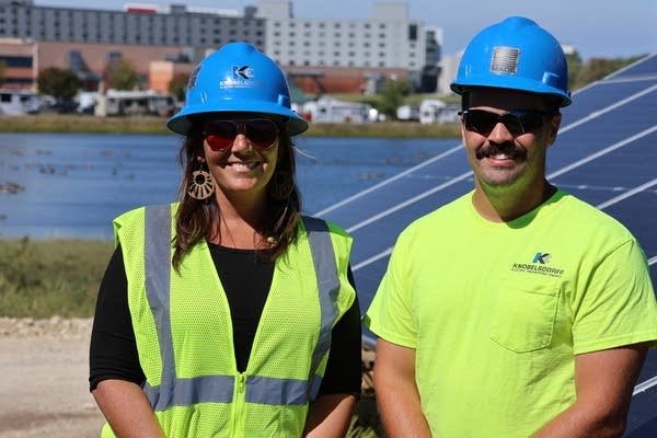 Two people in hard hats and high-visibility gear smile