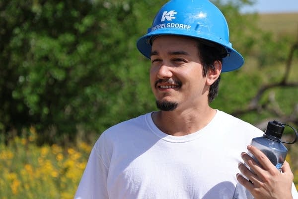 A man wears a hard hat and holds a water bottle.