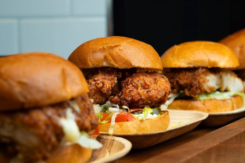 A row of fried chicken sandwiches on small wooden plates. 