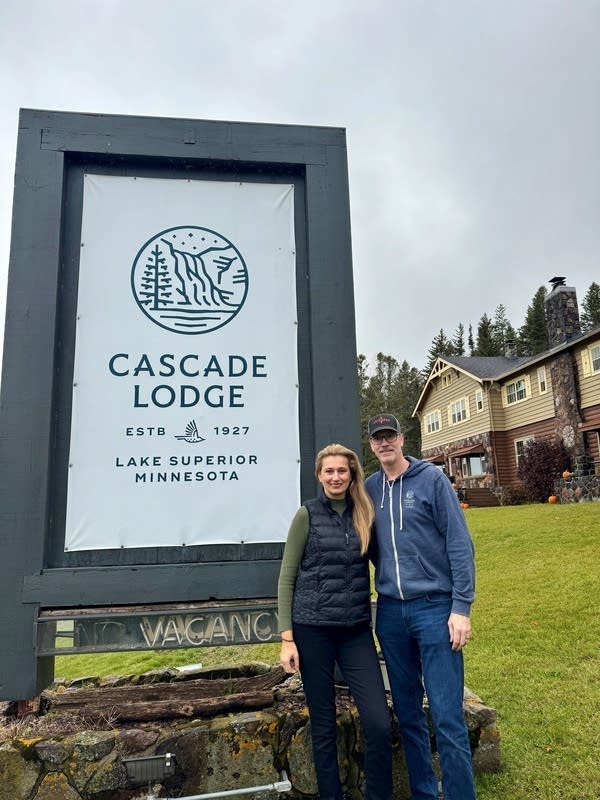Two people stand next to lodge sign