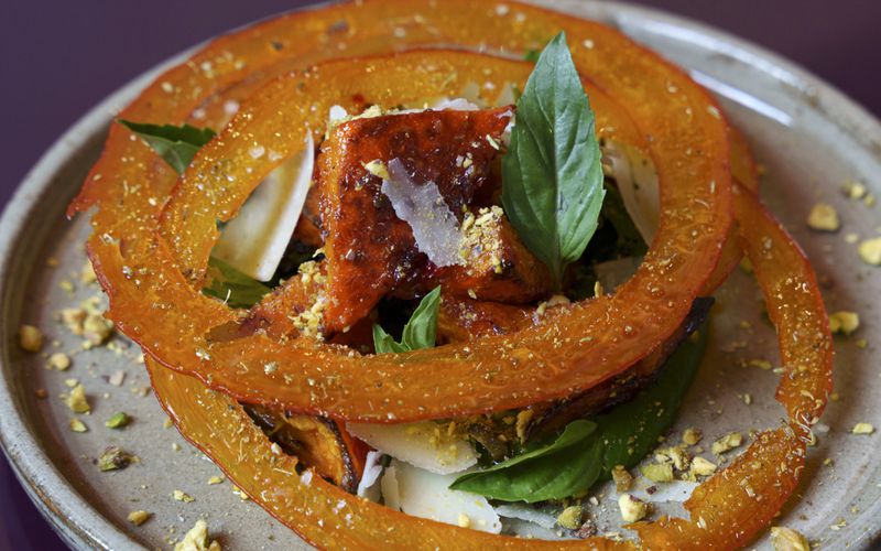 Rings of orange squash over chunks of squash, finished with shavings of Parmesean, basil leaves, and pistachios, with a kale puree beneath the squash. 