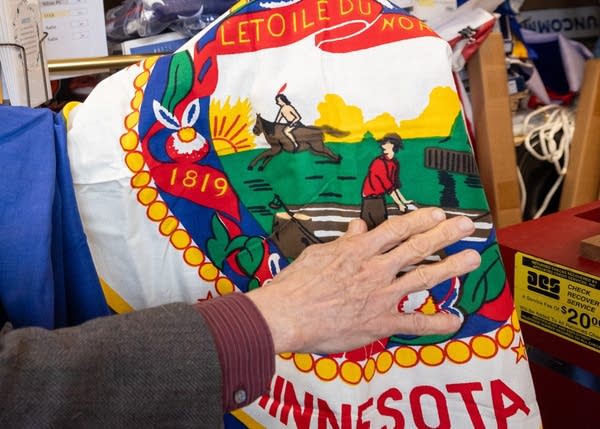 A hand rests on the current Minnesota state flag.