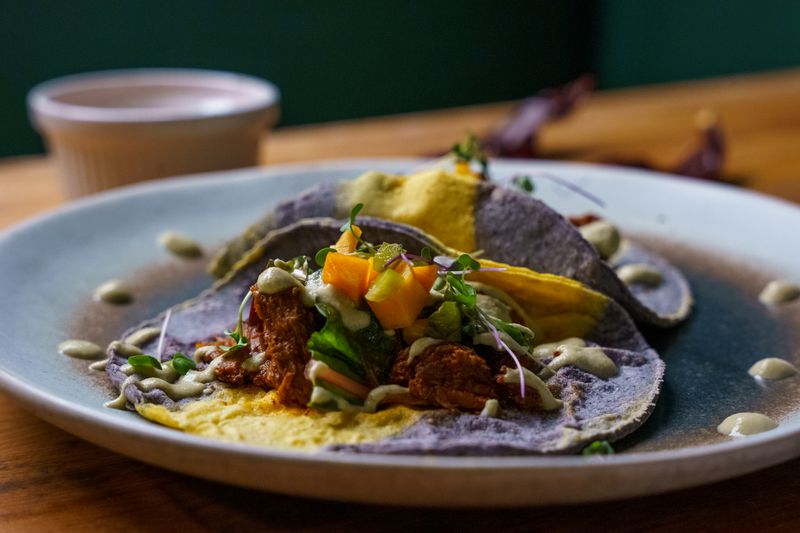 Blue and yellow corn-striped corn tacos with meat, squash, and greens on a stone plate. 