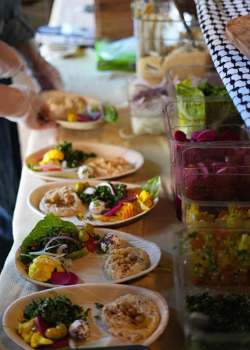 A number of plates with hummus and vegetables on a long table. 