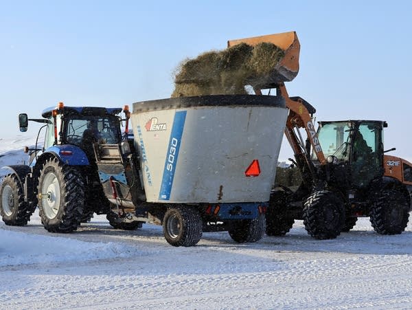 A front end loader dumps hay into a trailer