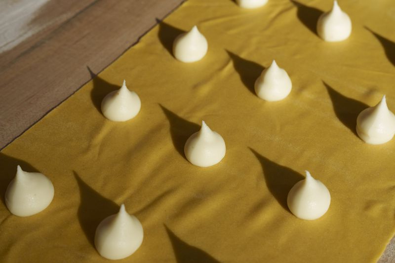 Domed dollops of a creamy white parmesan butter filling on a thin long pasta sheet. 