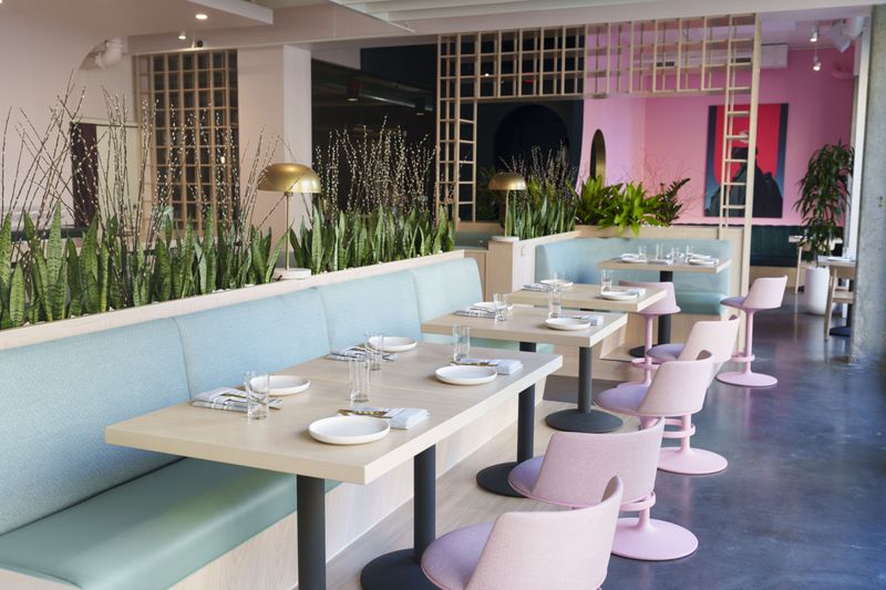 A long light blue banquette with blonde wood tables in font of it, and light pink chairs.