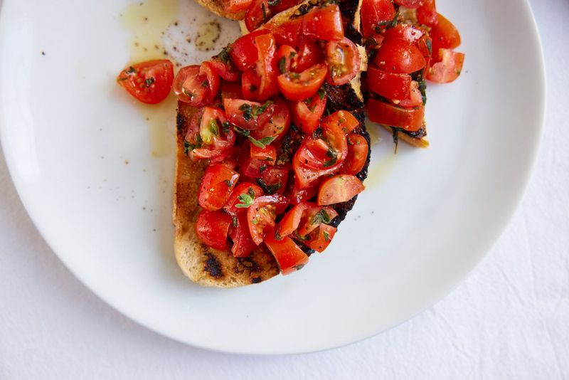Tomato bruschetta drizzled with olive oil on a white plate. 