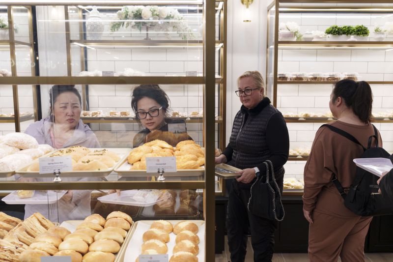 Four people holding trays milling in Keefer Court Bakery, selecting pastries from glass cases with gold trim.