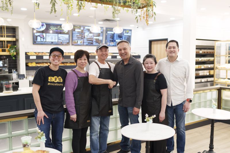 Michelle, Paulina, and Sunny Kwan; Michael and Mai Bui, and Peter Do standing together in Keefer Court Bakery, smiling as Sunny and Michael shake hands.