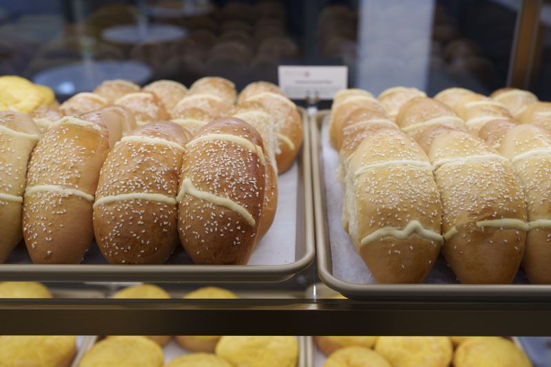 Rows of golden coconut custard buns dusted with sesame seeds on silver trays with white sheets of paper.