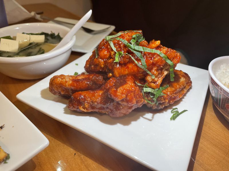A square white plate of gochujang chicken wings on a wooden table. 