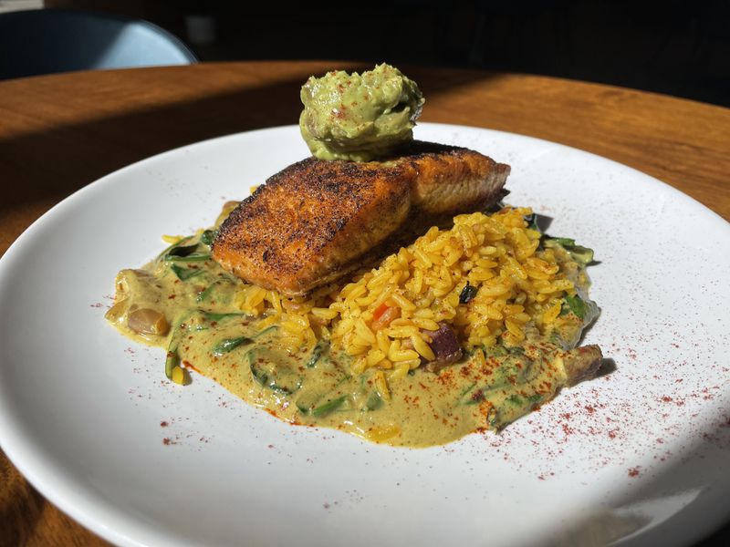 Spiced salmon over a bed of curry braised kale and yellow rice. topped with avocado mousse. 
