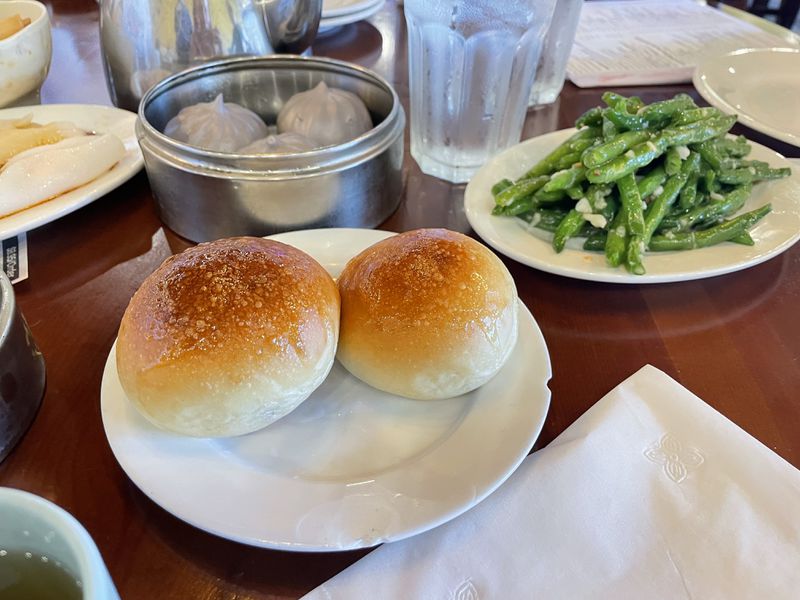 Two golden round buns and a plate of green beans on a wooden table. 